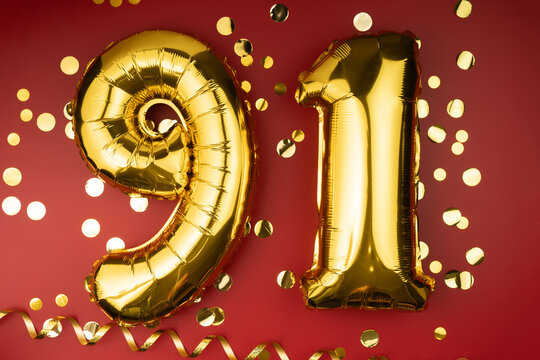 91st birthday celebration. Gold festive balloons number 91 year anniversary on red background with confetti. Birthday or wedding event.