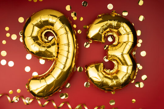 93rd birthday celebration. Gold festive balloons number 93 year anniversary on red background with confetti. Birthday or wedding event.