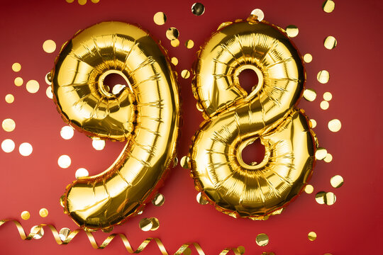 98th birthday celebration. Gold festive balloons number 98 year anniversary on red background with confetti. Birthday or wedding event.