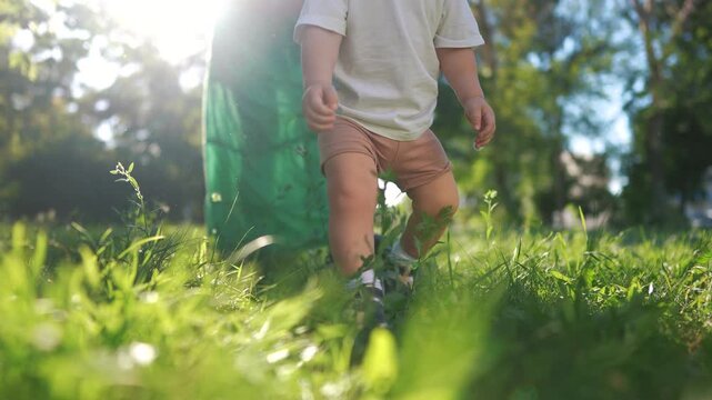 A baby is taking the first steps on its legs. Child step family concept. Baby learns to walk in the park. Baby learns to walk with her legs in the lifestyle park.