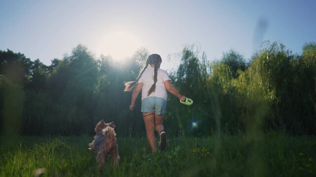 Dog is running on grass with a child. pet family kid concept. daughter runs on the grass with the dog in the park. a child and a dog on a leash run on green grass, lifestyle glare of the sun.