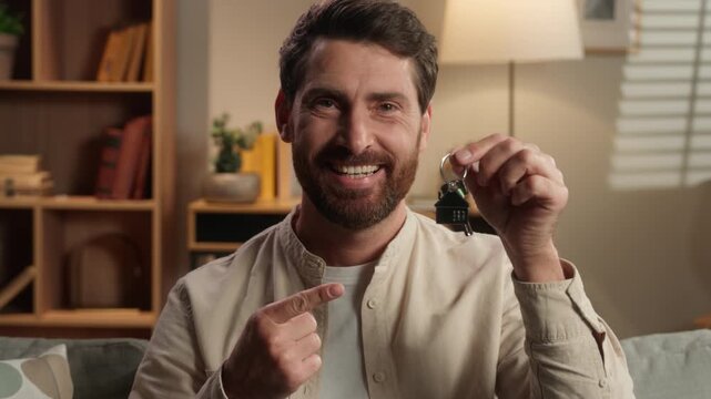 Close up middle-aged Caucasian man smiling happy showing with index finger at bunch of key looking at camera headshot male smile in home renting new apartment rent flat residential dwelling moving day