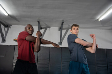 Stretching two partners in red, gray shirts warming up in dojo, with wall pads and lights © wavebreak3