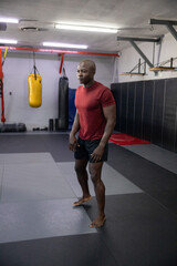 Mature African American man standing barefoot on mats in gym wearing red shirt facing heavy bags © wavebreak3