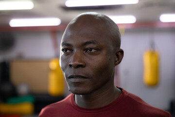 Mature African American man standing in gym wearing maroon athletic shirt near yellow punching bag © wavebreak3