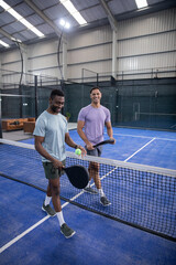 Two men holding paddles at net, left player holding ball, initiating sports rally on blue court © wavebreak3