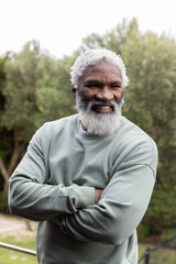 Senior African American man smiling arms crossed outdoors wearing sage crewneck necklace by railing © wavebreak3