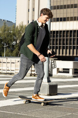 Teenage male skateboarding across urban rooftop plaza pushing off holding smartphone and backpack © wavebreak3