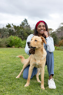 Adult Asian woman kneeling on lawn at park wearing red headband holding golden dog collar, smiling