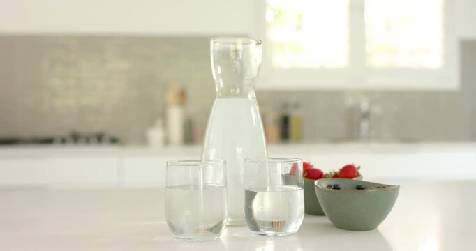 Slow camera tightening on carafe and glasses on kitchen counter, emphasizing green berry bowl