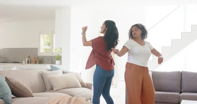 Dancing two women moving together in living room, one wearing rust red shirt other holding remote