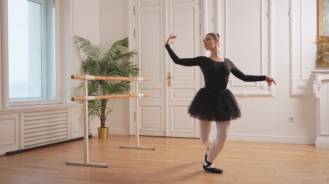 Young ballerina in tutu skirt stretching practicing ballet positions dancing near ballet barre in dance class. Young classical dancer woman in dance studio. Ballet class training Ballet school concept