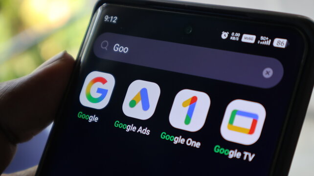 A hand holding a smartphone with Google apps on the screen