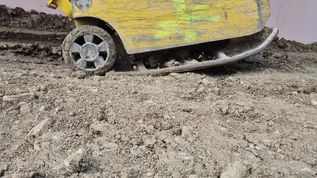 Slow motion side view of a plate compactor vibrating and leveling the uneven ground