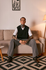 Fototapeta premium Handsome young man dressed in stylish attire sits on a sofa in a warm, cozy room