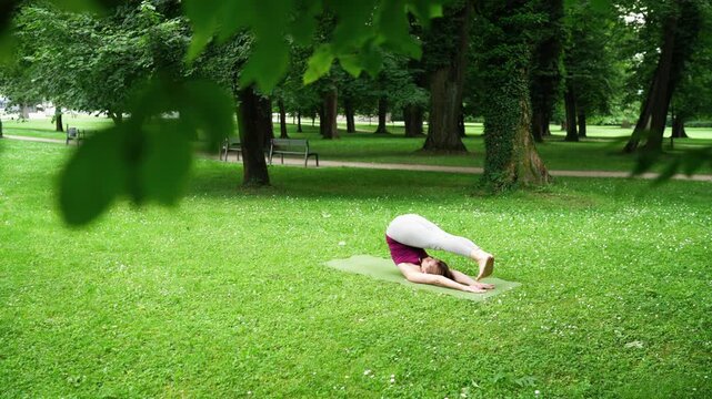 Woman practicing yoga in serene forest doing Plough Pose and Urdhva Mukha Paschimottanasana stretch on green lawn. Peaceful environment for focus and connection with nature in outdoor setting. 4K