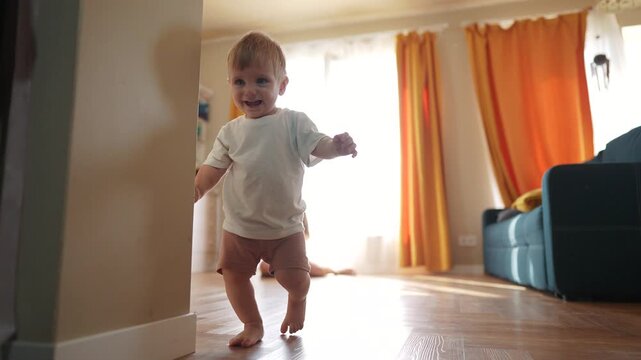 The first steps baby of learning to walk in home. Child toddler family concept. A baby is taking the first steps on its legs. A baby takes the first steps on lifestyle his legs at home.