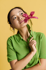Young woman in stylish green attire holds a flower against a vibrant yellow backdrop