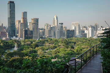 Obraz premium The view of the Bangkok skyline from Lumpini Park shows a lush green urban landscape and modern skyscrapers, including a bridge in Dusit Central Park, Bangkok, Thailand.
