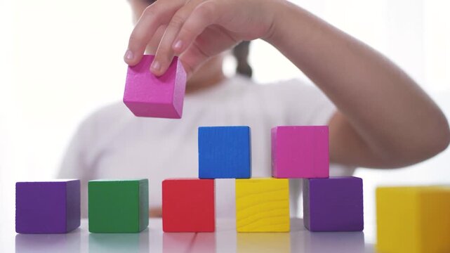 A girl plays with blocks and toys in kindergarten. Constructor little child concept. The girl daughter is playing with cubes. Girl collects toys from a lifestyle stack of cubes.