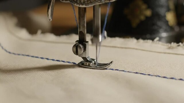 Close-up of vintage sewing machine needle stitching blue thread into white fabric, crafting a straight seam