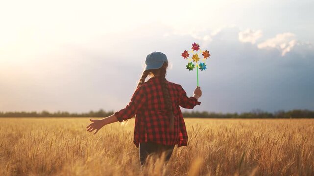 A girl running around with a pinwheel. Summer happy wind concept. A kid runs a windmill with wheat. A child's daughter runs and plays through a field of wheat at sunset. family childhood concept fun.