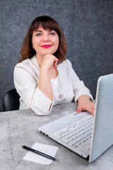 A brunette woman, 40-50 years old, at a desk with a laptop and a calculator