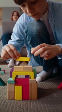 Young boy builds colorful wooden house from blocks on carpet