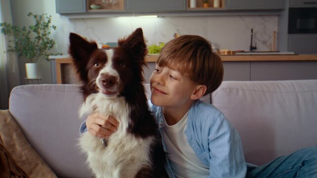 Young boy hugs dog smiling during close moment on sofa at home