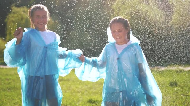 Children in raincoats play in the rain together and enjoy the summer. Cheerful family concept for child. Children playing in the rain outside. Children in raincoats play together lifestyle in nature.