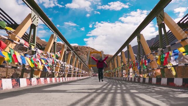 Teenager girl running and jumping with joy on Chicham bridge at Spiti Valley, India. Tourist enjoying summer vacation in Indian Himalayas and exploring Asia's highest suspension bridge. Travel concept