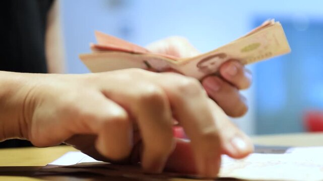 Hands counting Thai banknotes while pointing at a document on a desk, representing financial planning, payment, budgeting, money, cash, and personal expense management