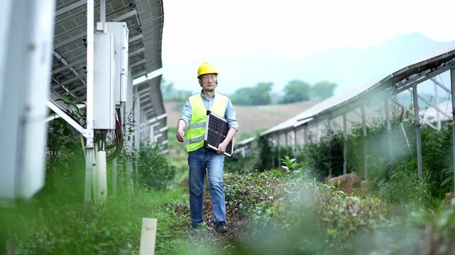 Engineer inspecting photovoltaic power station while holding a solar panel in rural field