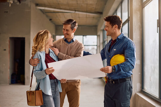 Happy homeowners analyzing blueprints with construction worker during home remodeling project.