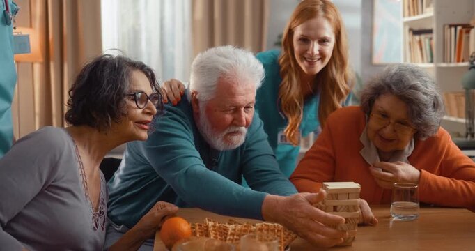 Seniors playing wooden block stacking game in assisted living home, laughing and enjoying social time together. Fun, excitement and friendly interaction indoors.