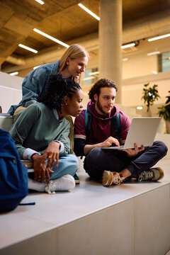 Diverse college friends surfing the net on laptop at lecture hall.