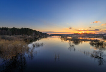 Fototapeta premium Golden sun dips low over calm lake surface