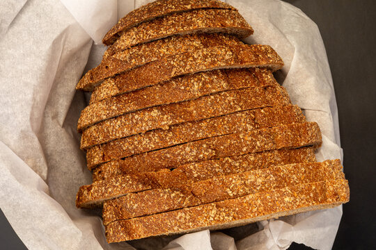 Sliced artisanal rye or whole grain bread in a paper-lined basket on a dark background
