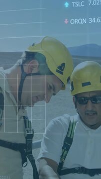 Vertical video: Two site technicians in helmets checking data, overlays appearing for safety