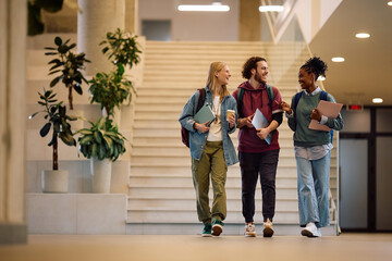 Naklejka premium Happy diverse students talking while walking through university hallway.