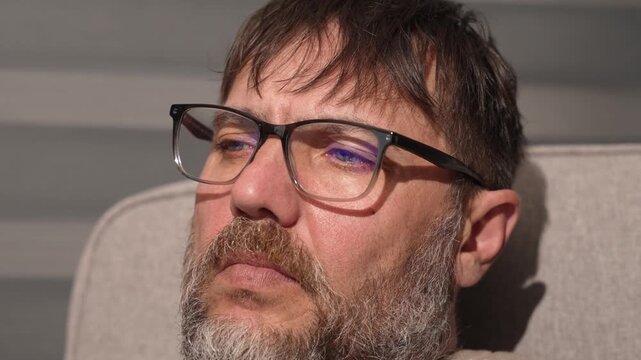 Bearded man with glasses in deep thought on sofa