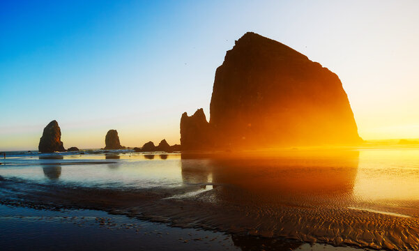 Sunset over Cannon Beach, Oregon. Vibrant sky, ocean waves, and the iconic Haystack Rock silhouetted against the evening light.