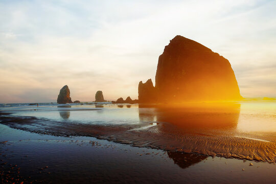 Sunset over Cannon Beach, Oregon. Vibrant sky, ocean waves, and the iconic Haystack Rock silhouetted against the evening light.