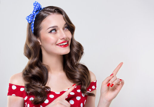 A Pin Up young smiling woman in a retro outfit points to the side, showcasing an invisible Presenting your product .Beautiful vintage girl with curly hair  .Expressive facial expressions
