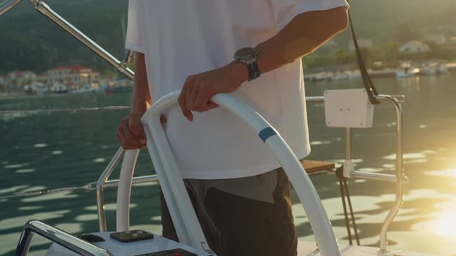 Caucasian Helmsman Hands On Wheel, Golden Sunset Glow Reflecting On Calm Water, Closeup Of Wristwatch And Firm Grip, Careful Course Adjustment While Approaching Quay