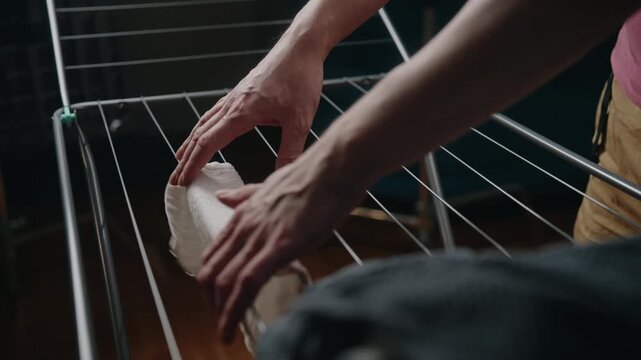 Closeup of male hands hanging clean, wet clothes and towels on collapsible metal drying rack indoors, performing daily household chore and practicing energy conservation. Concept of hygiene.