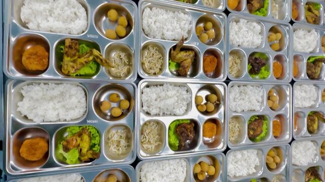 Mass-produced meals on individual compartment trays, featuring rice, chicken, and vegetables, ready for serving or distribution