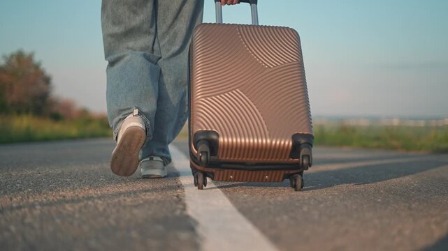 Woman walking alone with suitcase on road. Traveler drags luggage on asphalt path. Journey starts for traveler walking forward. Road adventure for traveler with suitcase. Man journey on long road.