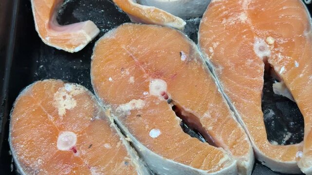 Chilled Atlantic salmon steaks piled, glittering ice crystals on raw orange fillets on black tray, retail display vibe, cold.