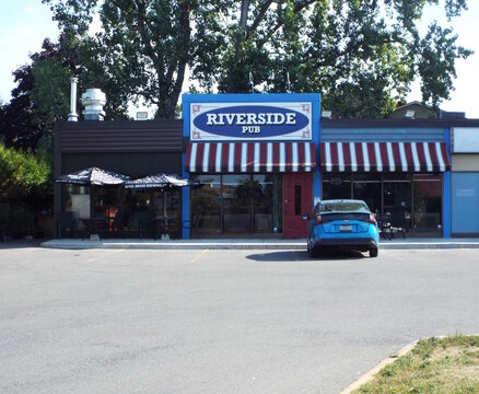 Ottawa, Ontario, Canada &ndash; July 26, 2025: The exterior of "Riverside Pub" features a blue facade, striped awnings, a patio, and a blue car parked at 3673 Riverside Dr.
